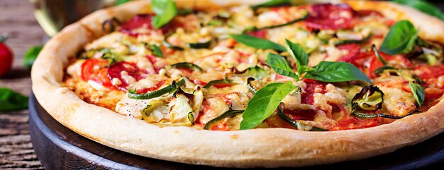 Pizza con pollo, salame, zucchine, pomodori ed erbe sul tavolo di legno d'epoca. . banner. cucina italiana