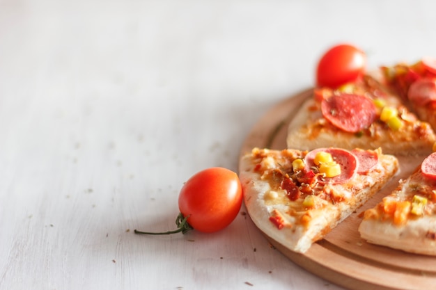 Pizza with corn, sausage, tomatoes on a wooden round board