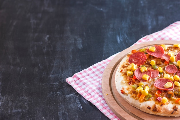とうもろこし、ソーセージ、トマトの木の丸い板のピザ