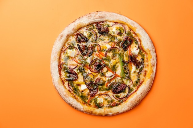 Пицца с вялеными помидорами фета, болгарским перцем, луком, песто и моцареллой, апельсиновый фон, вид сверху, копия пространства