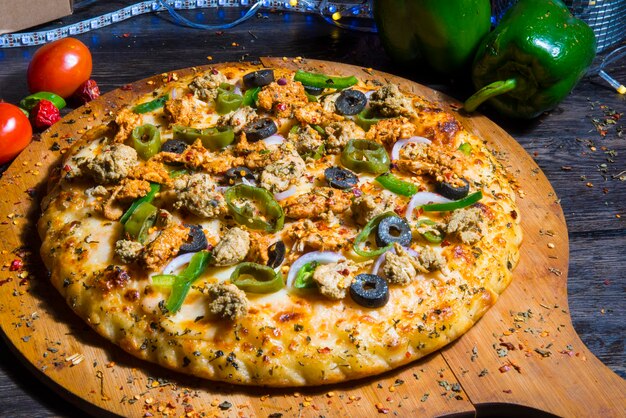 Photo a pizza with green peppers and black olives on a wooden board