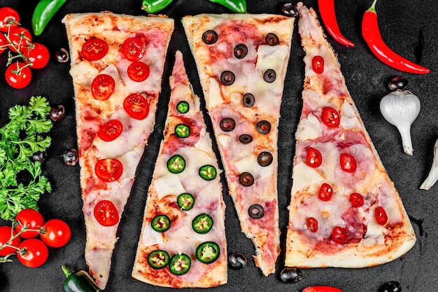 Pizza with ham mozzarella tomatoes olives and hot pepper on a black background top view