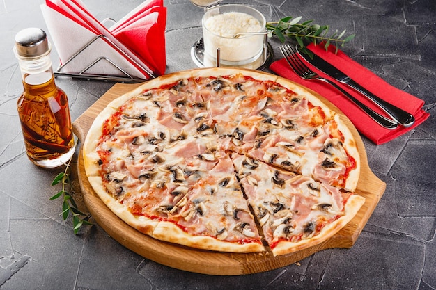 Pizza with ham and mushrooms on wooden board on dark background Closeup