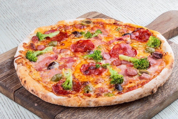 Pizza with ham sausages chorizo broccoli and olives on a wooden board