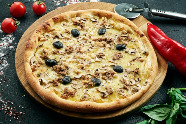 Pizza con un gran numero di condimenti: tonno, cipolla, funghi, olive, formaggio e peperone. pizza in composizione con ingredienti su un tavolo nero