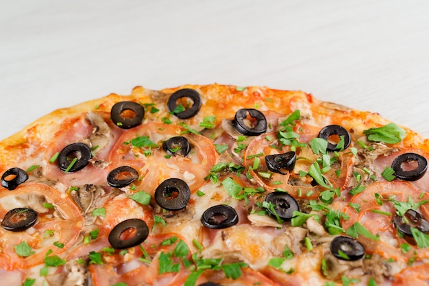 Pizza with meat, olives, tomatoes, mushrooms, herbs isolated on white wooden surface