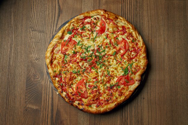 Pizza with melted cheese and tomato on a wooden tray. Pizza in composition with ingredients on a wooden table. Top view.