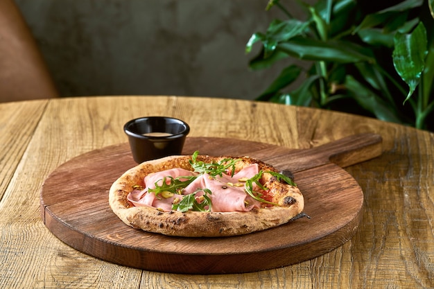 Pizza with mortadela, arugula and pistachios on a wooden board. Italian Cuisine