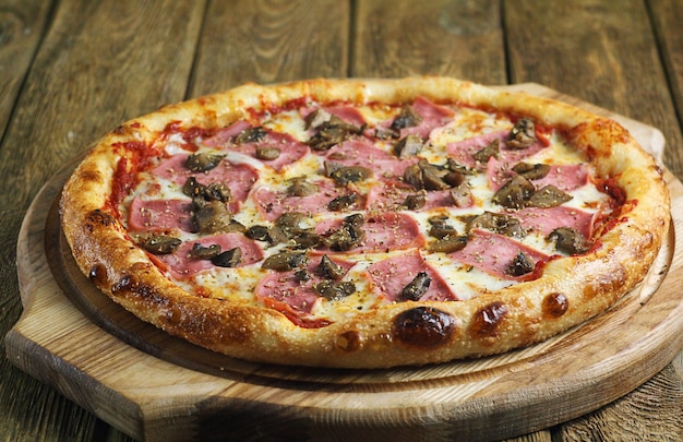 Pizza with mushrooms ham and tomato paste lies on a wooden board on the table