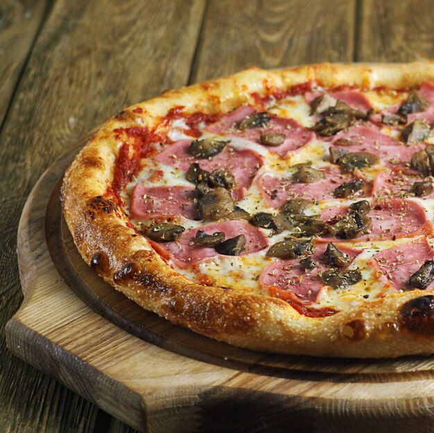 Pizza with mushrooms ham and tomato paste lies on a wooden board on the table