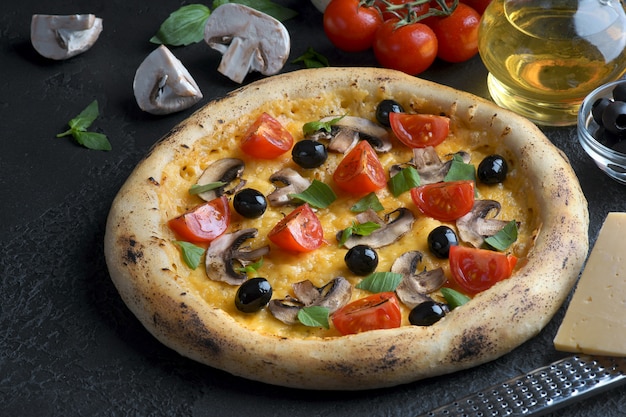 Foto pizza con funghi, pomodori e olive su uno sfondo scuro