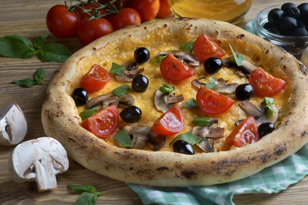 Pizza con funghi, pomodori e olive su uno sfondo di legno