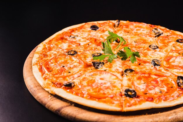 Pizza with olives and tomatoes on a wooden board on a black background