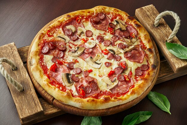 Pizza with pepperoni salami, melted cheese, mushrooms and chili pepper on wooden tray.