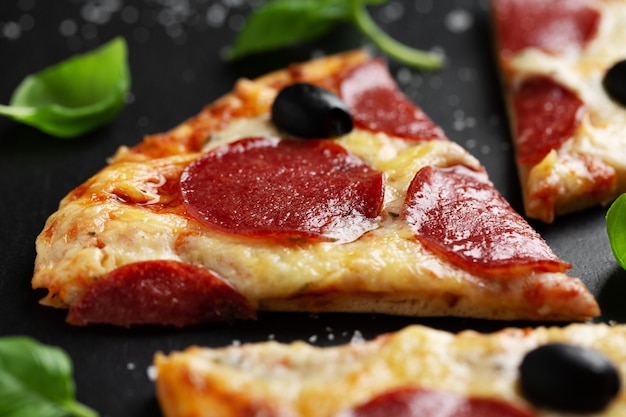 Pizza with salami and cheese on dark surface