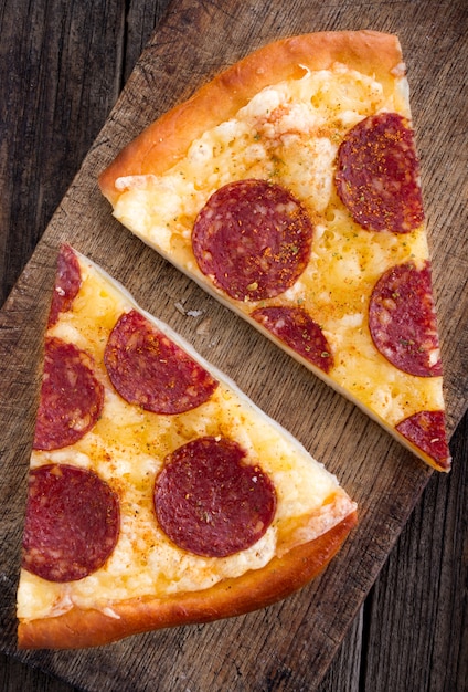 Pizza with salami on old wooden background.