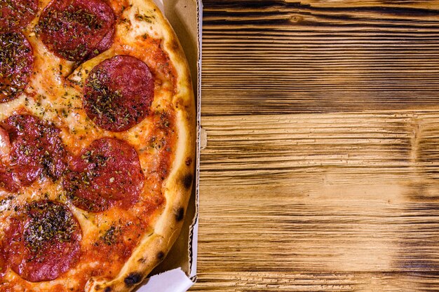 Pizza with salami sausage and parmesan cheese in cardboard box on a wooden table. Top view