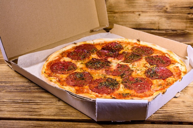 Pizza with salami sausage and parmesan cheese in cardboard box on a wooden table