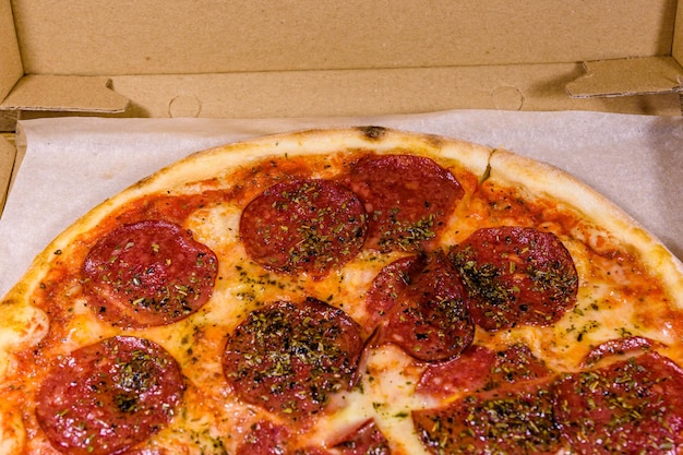 Pizza with salami sausage and parmesan cheese in cardboard box on a wooden table