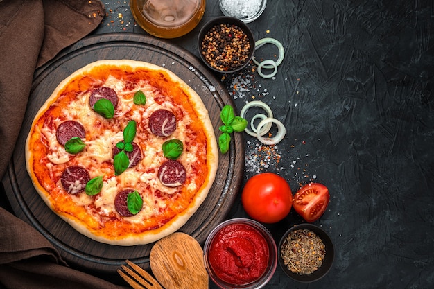 Pizza with salami, tomatoes and cheese on a black background.