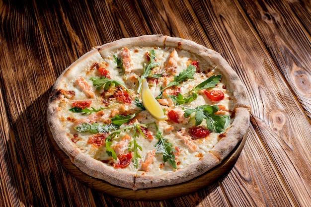 Pizza with salmon mozzarella cherry tomatoes arugula lemon and parmesan Italian cuisine on a woden background