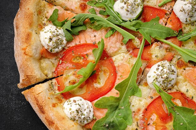 Pizza with salmon tomatoes cheese and spices on a dark background