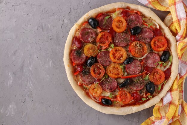 Pizza with sausage, tomatoes, mozzarella and black olives on a gray background, Top view, Copy space