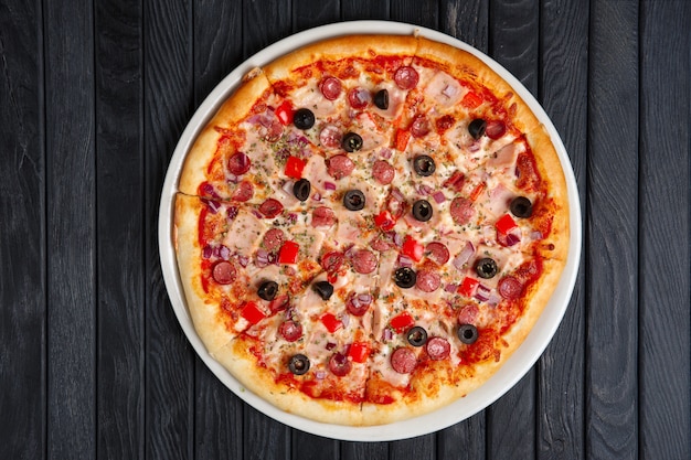 Pizza with thin sausage, bell pepper, ham and black olives