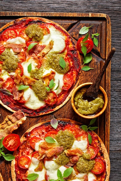 Foto pizza con pomodori, mozzarella, pancetta fritta croccante e salsa al pesto su una tavola di legno rustica e maleducata, vista verticale dall'alto, piatta,