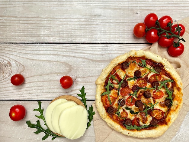 Pizza with tomatoes, parmesan cheese and herbs, beige towel on wooden background. Top view, flat lay