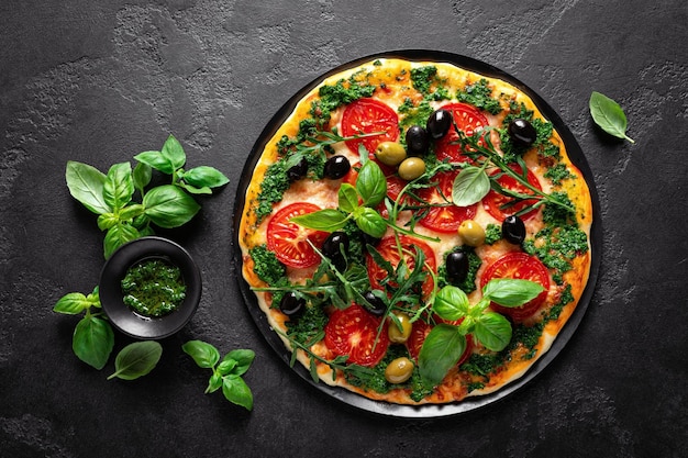 검정색 배경에 토마토, 시금치, 올리브가 있는 피자.