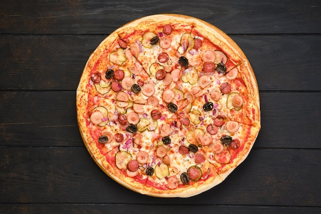 Pizza with various kind of thin sausages pickled cucumber olives and onion