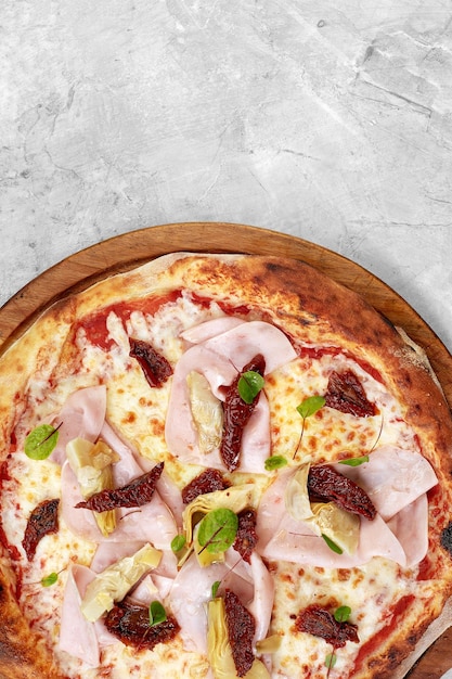Pizza with veal ham cheese and sundried tomatoes on a gray table