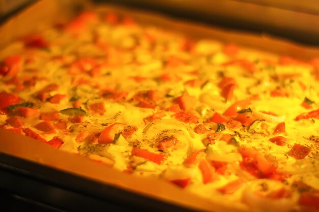 Pizza with vegetables and meat baking in the oven