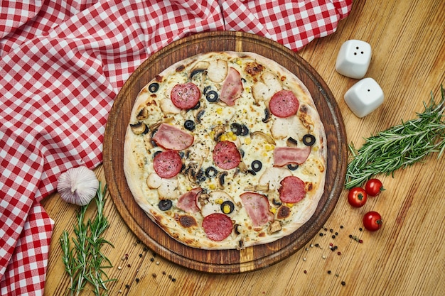 Pizza with with smoked chicken, ham, salami, olives and white sauce on wooden tray.