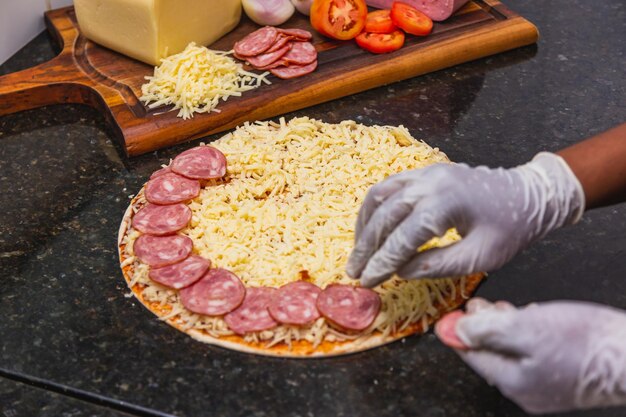 Pizzabereiding die pepperoniringen en plakken op pizzadeeg uitspreidt verse pizza-ingrediënten op houten plank