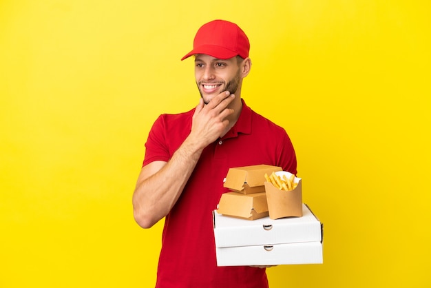 Pizzabezorger die pizzadozen en hamburgers ophaalt over een geïsoleerde achtergrond die naar de zijkant kijkt en glimlacht