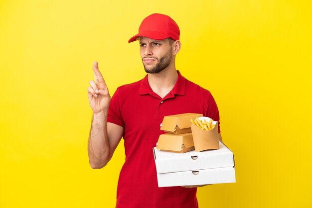 Pizzabezorger die pizzadozen en hamburgers ophaalt over een geïsoleerde achtergrond met vingers die kruisen en het beste wensen