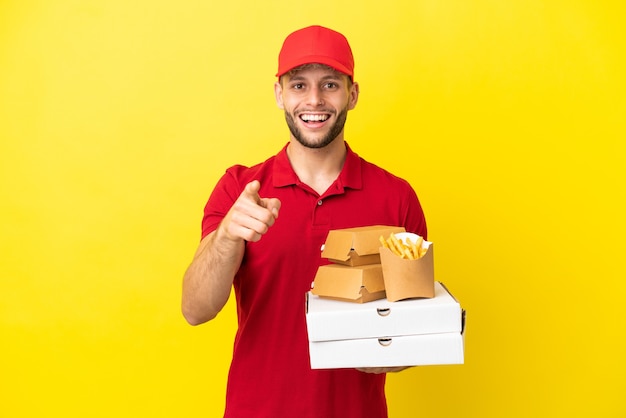 Pizzabezorger die pizzadozen en hamburgers ophaalt over een geïsoleerde achtergrond, verrast en naar voren wijst