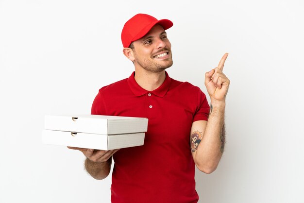 Pizzabezorger met werkuniform die pizzadozen ophaalt over een geïsoleerde witte muur die een geweldig idee naar voren wijst