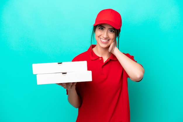 Foto pizzabezorger met werkuniform oppakken van pizzadozen geïsoleerd op blauwe achtergrond lachend