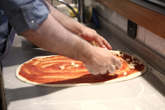 Foto pizzachef zet saus op basis in een commerciële keuken