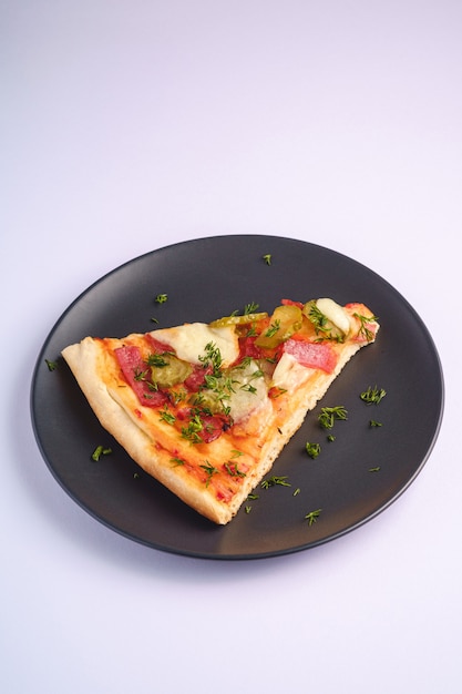 Pizzaplak met pepperoni, salami, gesmolten mozzarella, augurken en dille in zwarte plaat op witte achtergrond, hoekmening