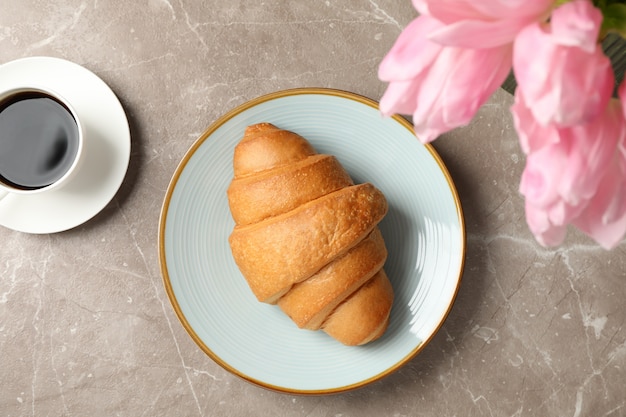 Plaat met croissant op grijze achtergrond met tulpen en kopje koffie, bovenaanzicht