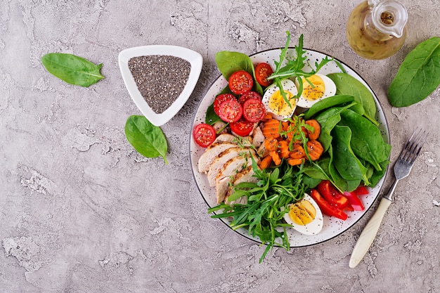 Plaat met een keto dieetvoedsel. Kerstomaatjes, kipfilet, eieren, wortel, salade met rucola en spinazie. Keto-lunch. Bovenaanzicht