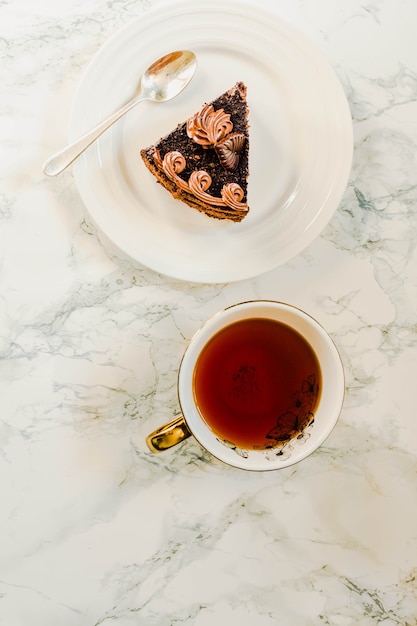 Plaat met plakje zelfgemaakte chocoladetaart en geelgouden kopje thee op marmeren achtergrond. Kopieer de ruimte. Bovenaanzicht. Kerst Nieuwjaar vakantie ontbijt concept