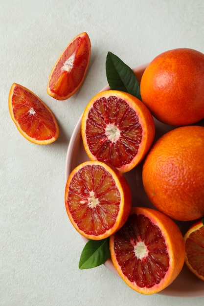 Plaat met rode sinaasappelen en bladeren op geweven wit