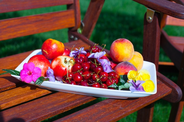 Plaat met vers fruit en bloemen op houten stoelen in de tuin