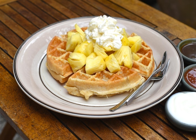 Plaat van Belgische wafels met ananas en ijs op een houten tafel