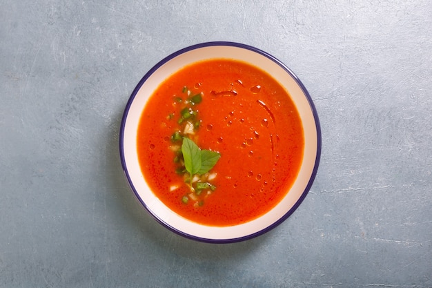 Plaat van gazpacho gemaakt van tomaat met knoflook en basilicum bladeren op grijze achtergrond kopie ruimte. Traditioneel Spaans gerecht